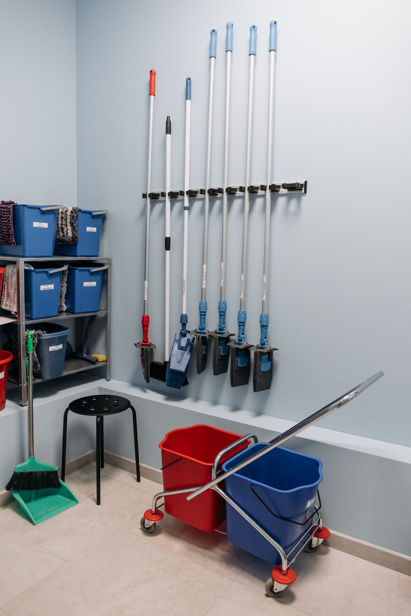 Mops, buckets, and cleaning supplies arranged on shelves in a storage room
